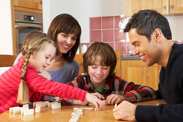Family Playing Dominoes In Kitchen Sitting Around Having Fun